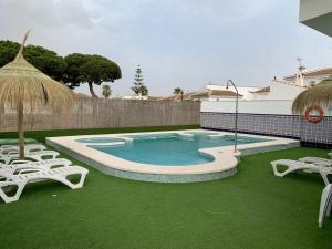 a swimming pool with two lawn chairs and an umbrella at Apartamentos Costa Luz in Matalascañas