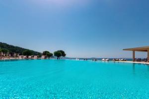 a large swimming pool with blue water and a beach at Ammoa Luxury Hotel & Spa Resort in Nikiti