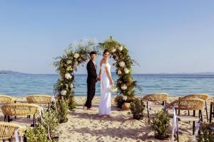 a bride and groom standing under a wedding arch on the beach at Ammoa Luxury Hotel & Spa Resort in Nikiti