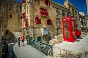 a red phone booth and a woman walking in front of a building at Central Family Apartment in Valletta