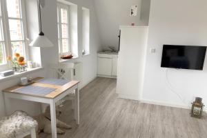 a white kitchen with a table and a tv on a wall at Doerpstraat 9_ Whg_ 8 in Wyk auf Föhr +2 photos