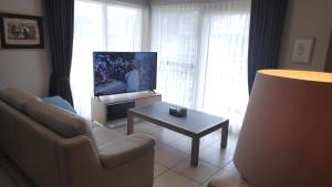 a living room with a couch and a tv and a table at Blutsyde Promenade Encanto in Bredene
