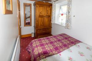 a bedroom with a bed and a wooden cabinet at Rosebud cottage Romantic cottage for a couple in Fishguard