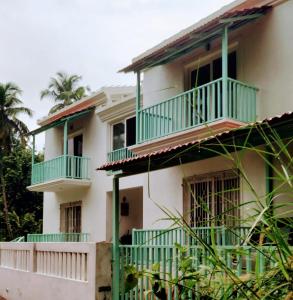 a white house with green balconies and palm trees at Beseco Bed and Breakfast in Benaulim