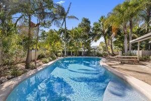 a pool with blue water in a yard with palm trees at Stylish Townhouse, private courtyard walk to beach in Noosaville