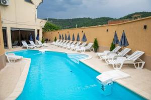 a swimming pool with white chairs and umbrellas at Хотел Дани in Sandanski