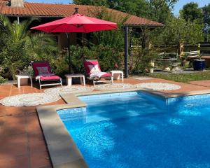 een zwembad met 2 stoelen en een rode parasol bij l'hacienda in Saint-Pierre-du-Mont