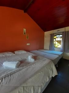 two beds in a room with an orange wall at Pousada Estalage in Cabo Frio