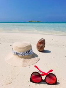 a straw hat and red sunglasses on the beach at Mystic Maldives Mathiveri Retreat in Mathiveri