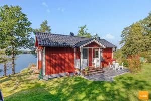 ein rotes winziges Haus mit einer Terrasse und einem See in der Unterkunft Ekudden. Idylliskt nära sjö. Egen strand. in Rimforsa