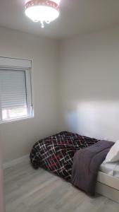 un lit dans une chambre blanche avec une fenêtre dans l'établissement Apartamento Aconchegante Esteio - Coração da Grande Porto Alegre, à Esteio
