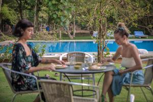 two women sitting at a table near a pool at PushkarOrganic - Lux farm resort with pool in Pushkar