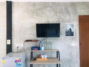 a television on a wall with a table and a refrigerator at SolarCell Private Homestay - โซล่าเซลล์ไพรเวทโฮมสเตย์ in Uthai Thani