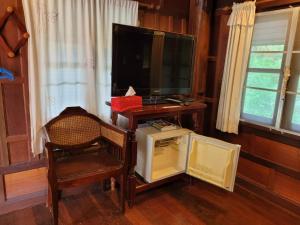 sala de estar con TV, silla y nevera pequeña. en Ruenthai Ampawa, en Samut Songkhram