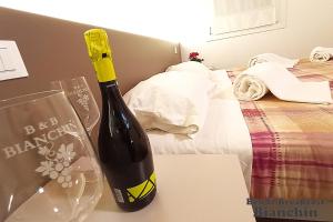 Una botella de vino sentada en una mesa junto a la cama en B&B Bianchin via Trieste 67 Fiumicello-Villa Vicentina, en San António