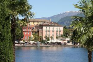 a river in front of a building with palm trees at Bellavista Hotel Deluxe Apartments in Riva del Garda