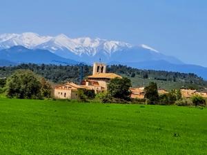 a church in a field with mountains in the background at Can Lluna Rural House in Avinyonet de Puigventós