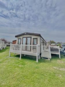 a small house with two white benches in the grass at Norfolk Caravan Staycation Pet Friendly in Belton