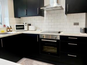 een keuken met zwarte kasten en een fornuis met oven bij Modern 4 Bedroom House with Parking in Wyken