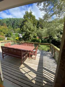 um deque de madeira com uma mesa e dois bancos em Twin Totara Cottage em Upper Hutt