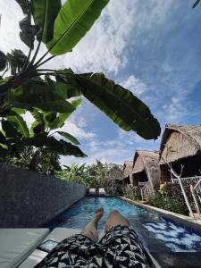 a person laying on a bed next to a swimming pool at HoneyBee Huts in Nusa Lembongan
