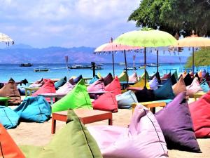 a bunch of colorful beach chairs with umbrellas on a beach at Gili Mesari Cottages & Homestay in Gili Trawangan