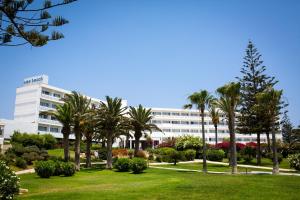 a building with palm trees in front of a park at Nissi Beach Resort in Ayia Napa