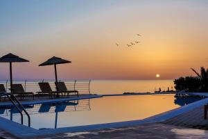 una piscina con sedie, ombrelloni e oceano di Romantica Beach a Hersonissos