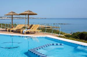 una piscina con sedie e ombrelloni accanto all'oceano di Romantica Beach a Hersonissos