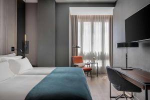a hotel room with a bed, chair, desk and a window at NH Collection Madrid Gran Vía in Madrid