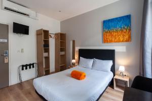 a bedroom with a bed with an orange pillow on it at Hotel l'Hotera in Cannes