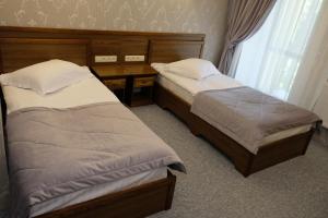 two beds in a bedroom with a desk and a window at Лісовий готель Гайки in Zhytomyr