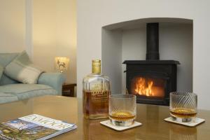 a bottle of whiskey and two glasses on a table with a fireplace at 1 Lower Spire in Dulverton
