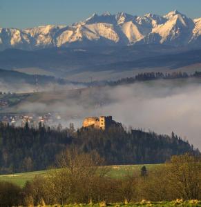 a building on a hill with fog in a field with mountains at Pokoje Gościnne Barka - 300m do RESTAURACJI - 900m do JEZIORA i VELO CZORSZTYN in Kluszkowce
