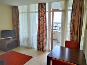 a living room with a table and a television and a window at Апартамент Сънсет Ризорт in Pomorie