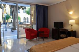 セビリアにあるサン ヒルの赤い椅子2脚とテレビが備わるホテルルームです。