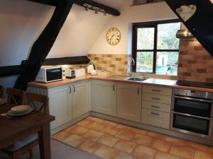 a kitchen with white cabinets and a clock on the wall at Penybont Barn in Llangorse