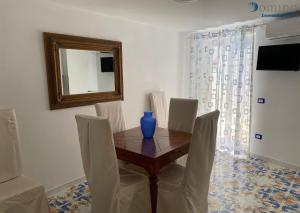 una mesa de comedor con sillas blancas y un jarrón azul. en Casa Fornillo, en Positano