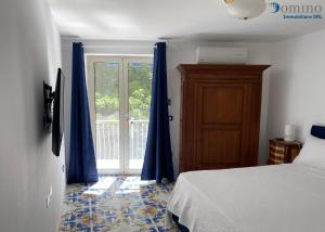 1 dormitorio con cortinas azules, 1 cama y ventana en Casa Fornillo, en Positano