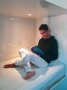 un hombre sentado en una cama sosteniendo un libro en HBB Hostel - Vila Madalena, en São Paulo