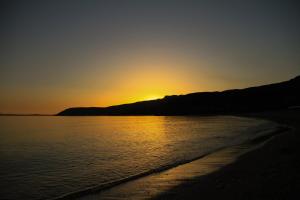 a sunset over a beach with the sun setting behind a mountain at Palataki in Kardamyli