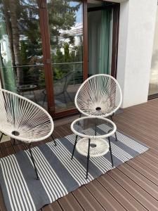 2 chaises blanches et une table sur une terrasse dans l'établissement Przytulny apartament, 200m od morza, Gdynia Orłowo, à Gdynia