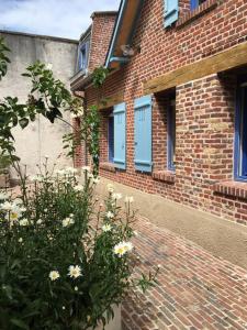 um edifício de tijolos com janelas azuis e um arbusto com flores em Margarita Apt Climatisé T2 4 pers Centre parking em Le Touquet-Paris-Plage