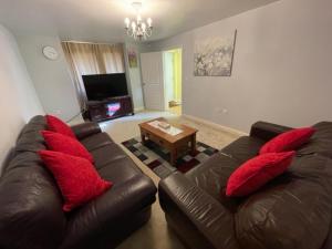 Holiday Home In Cardiff, Sleeps 8 في كارديف: غرفة معيشة مع أريكة جلدية بنية ومخدات حمراء