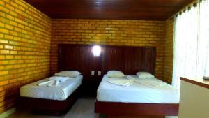 two beds in a room with a brick wall at Pousada do Forte in Barra do Cunhau