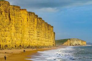 a large cliff next to a beach and the ocean at Cosy Flat in a Pretty Town. in Crewkerne