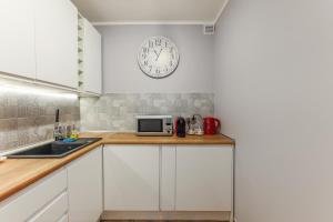 a kitchen with white cabinets and a clock on the wall at AP Apartments Piastowska in Gdańsk