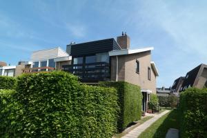 una casa con un seto verde al lado de un edificio en Dolfijn, Wijk de Brabander 92 en Cadzand