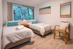 two beds in a room with a chair and a window at Beach & Trees, beachfront Siesta Park in Busselton