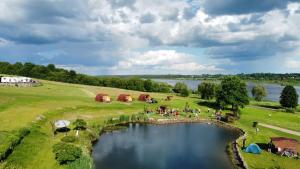 a group of people standing around a pond with tents at Camp Genys in Jurbarkas